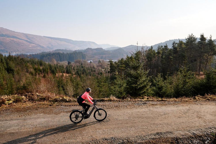 Rider on a Kalkhoff electric bike on a broad gravel track overlooking wooded hills.